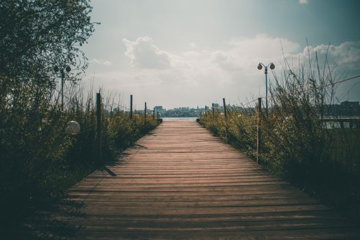 A tranquil wooden pathway leading to a scenic waterfront under a bright sky.