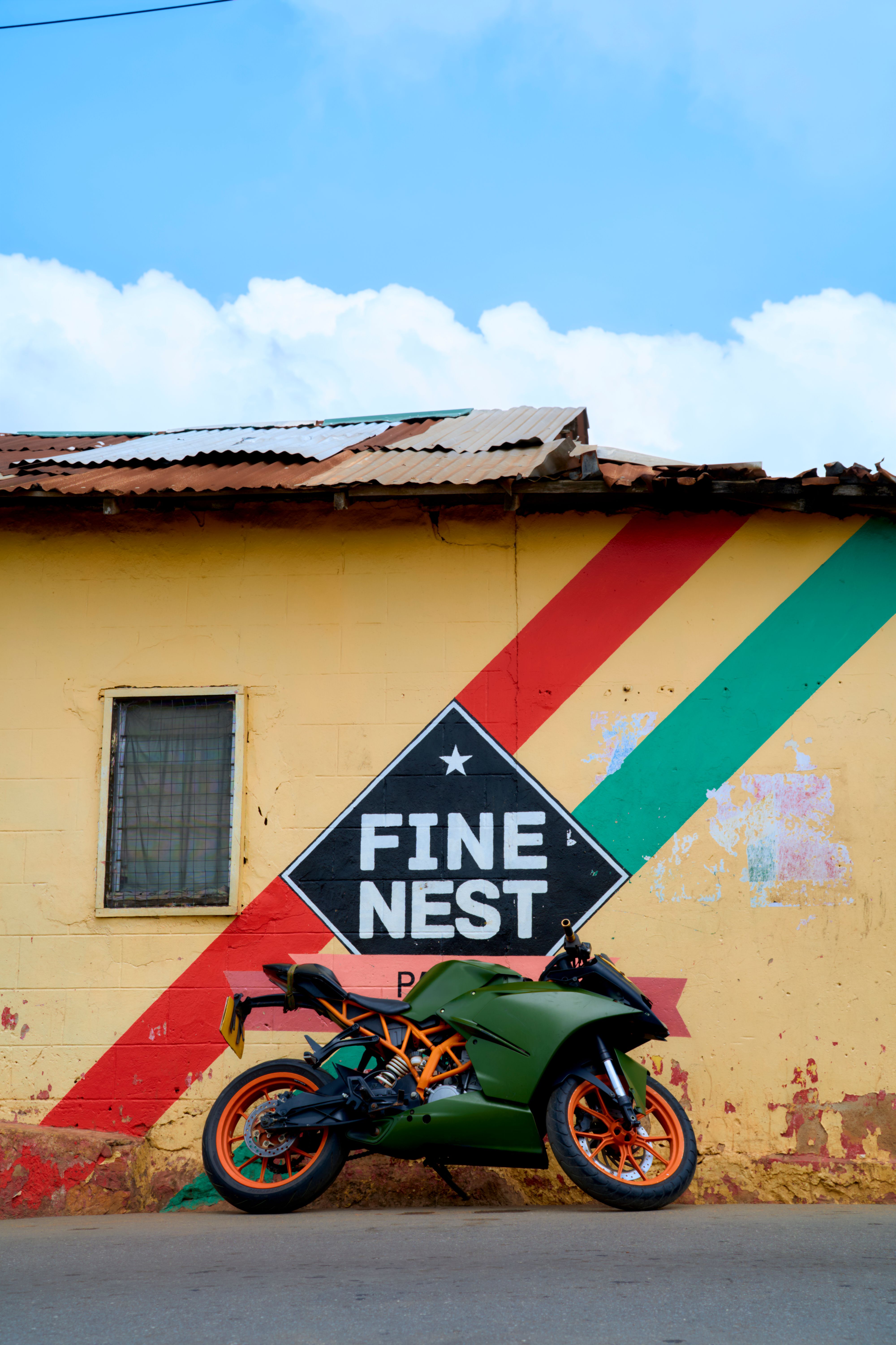 A green motorcycle parked outside a colorful painted wall in Aburi, Ghana.