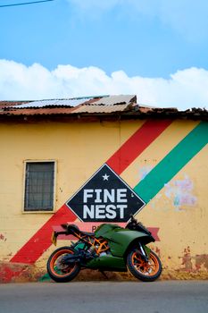 A green motorcycle parked outside a colorful painted wall in Aburi, Ghana.