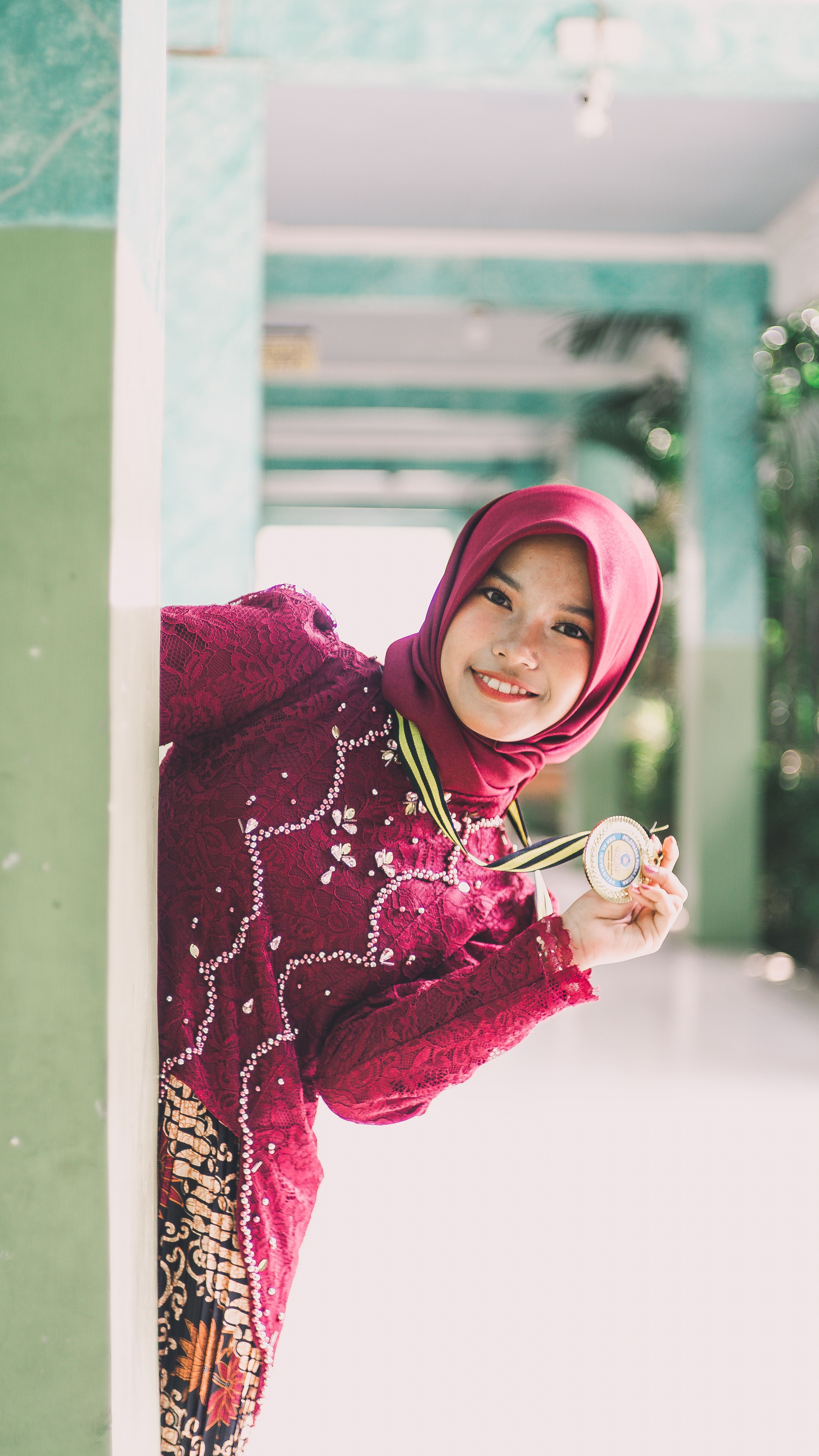 Smiling young woman wearing a hijab and traditional attire holding a medal, celebrating an achievement.