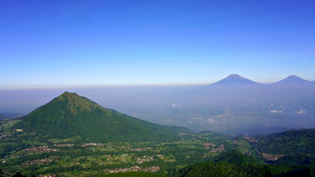 Panoramic view of green mountains under a clear blue sky, showcasing natural beauty. - Fotografer Sidoarjo