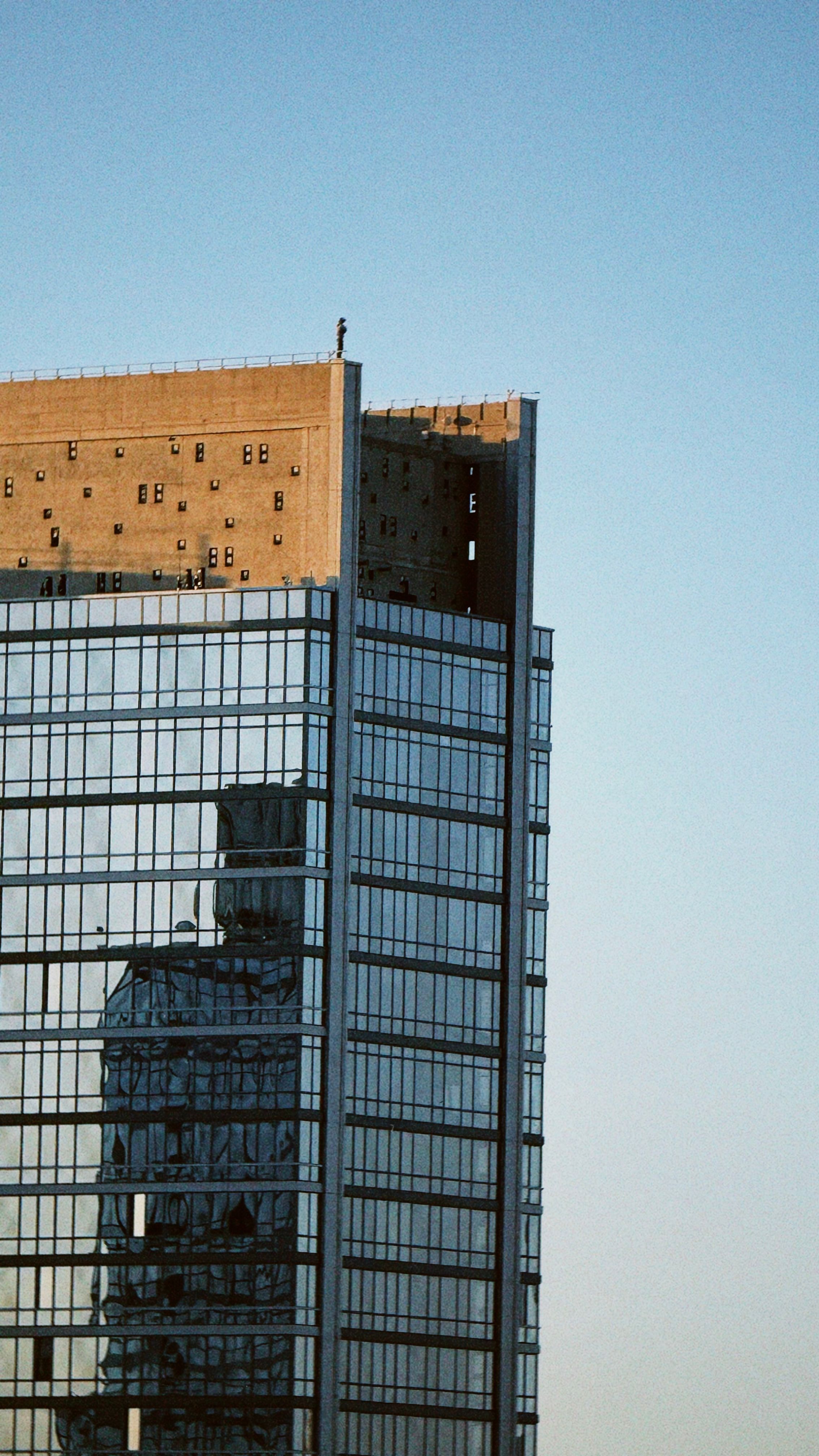 Glass skyscraper in New York reflects cityscape against a clear blue sky.