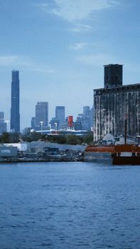 Cityscape at twilight with skyline and waterfront in foreground, featuring industrial buildings.