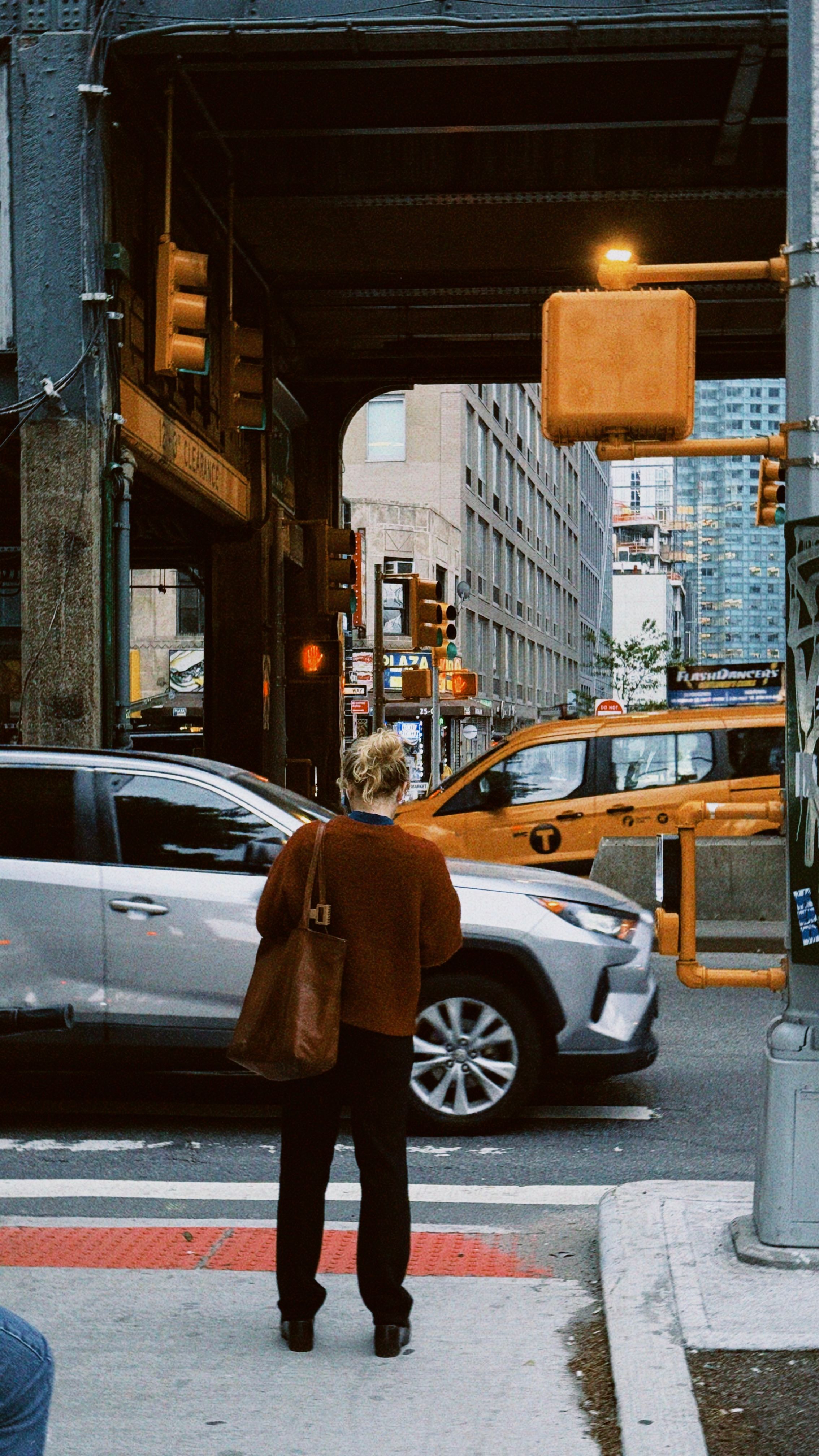 Person standing at a New York City intersection with traffic lights and taxis in view.