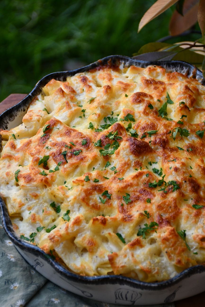 Golden-topped mac and cheese with visible pieces of shredded chicken and melted cheese, garnished with chopped chives in a white baking dish