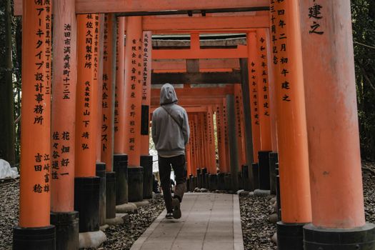Person walking through iconic orange torii gates at Fushimi Inari Shrine in Kyoto, Japan.