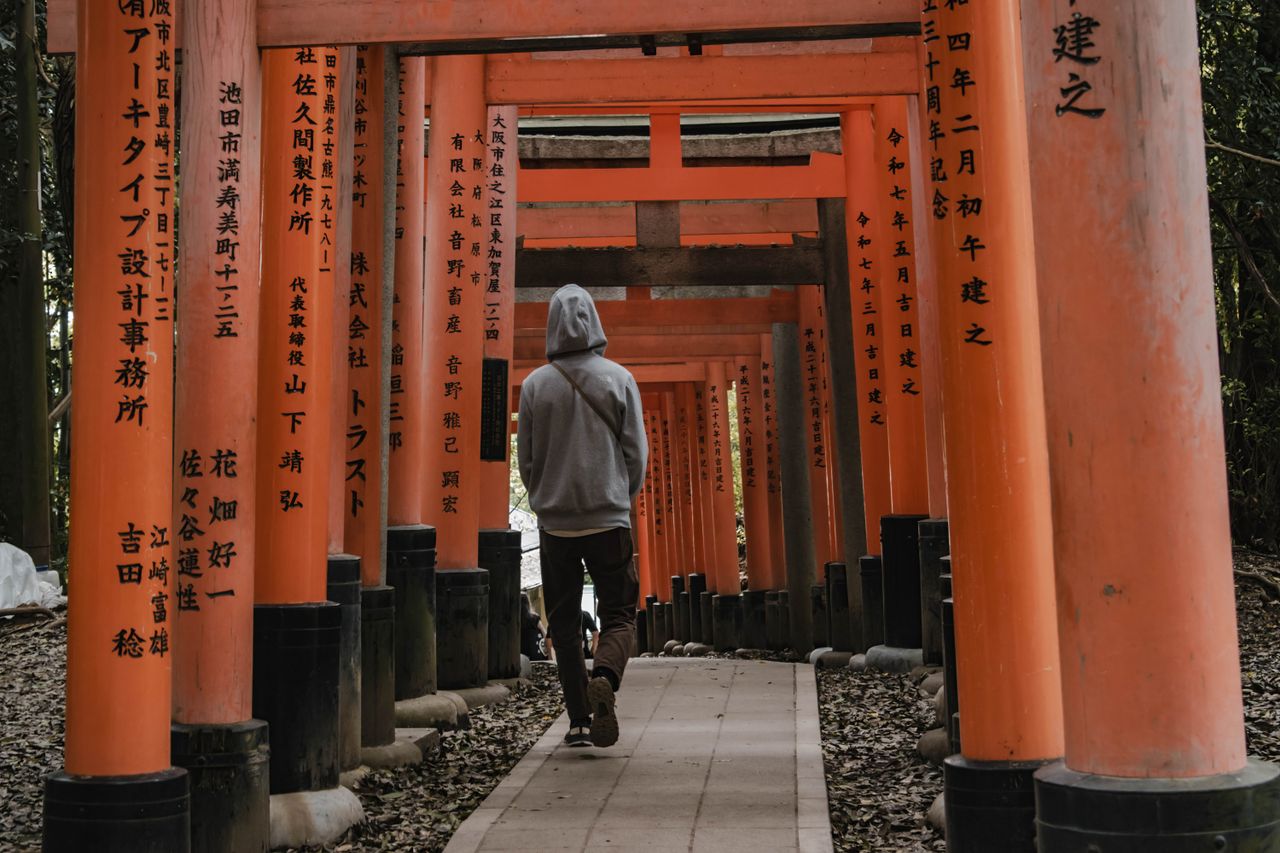 person walking through iconic orange torii gates at fushimi inari shri