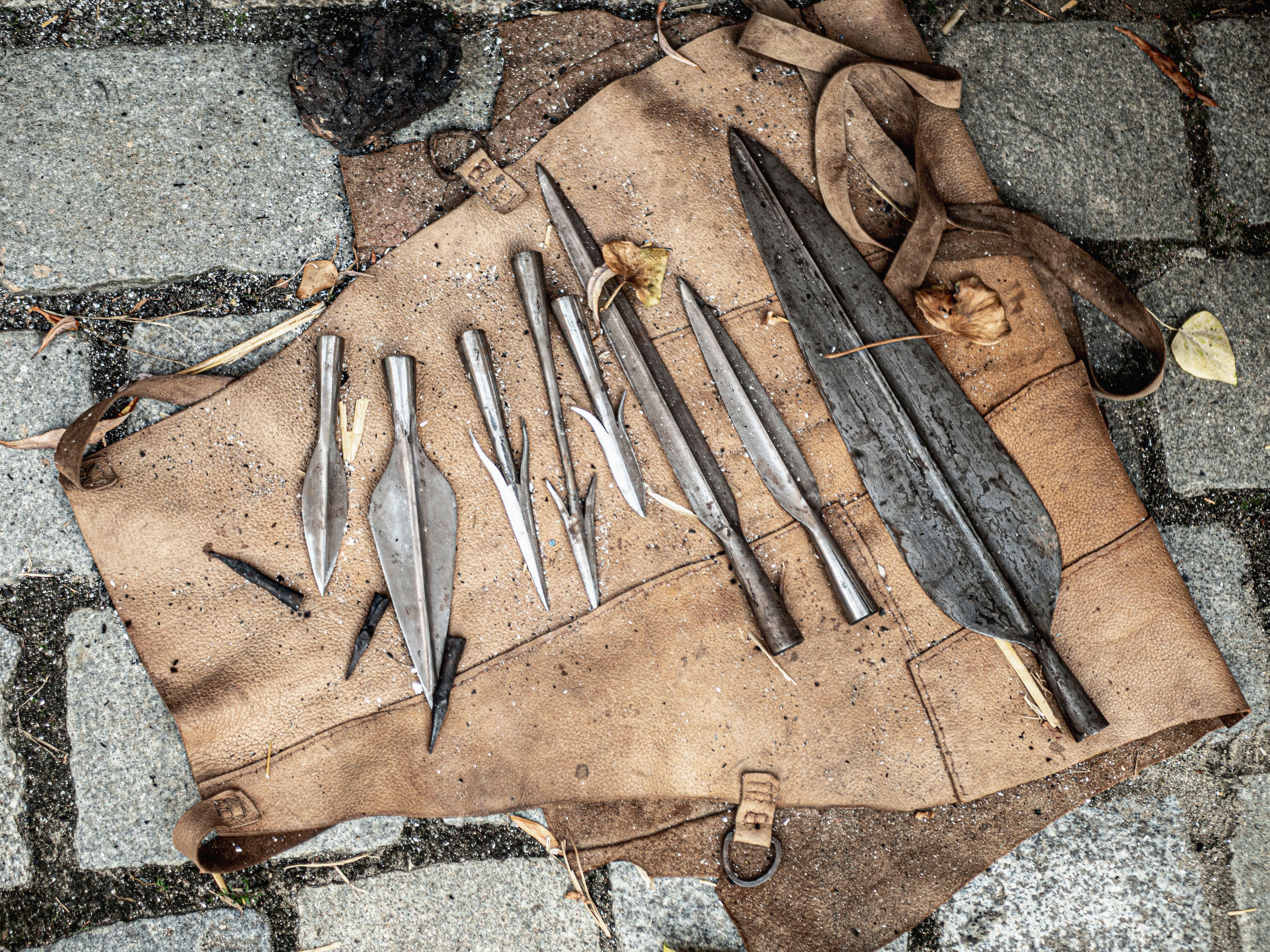 Vintage metal spearheads displayed on a worn leather mat on a stone pavement.