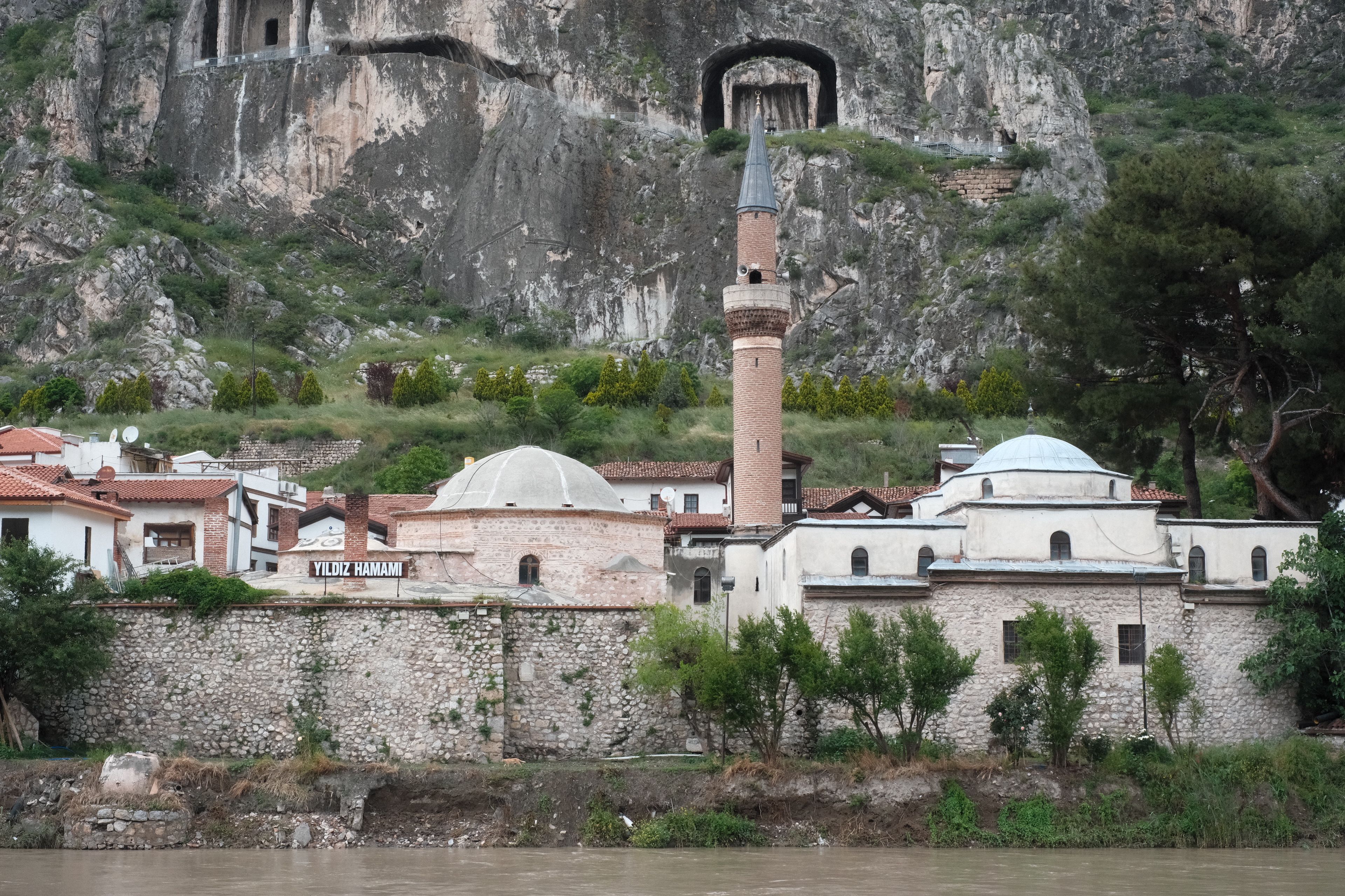 A scenic view of Yildiz Hamami and a mosque set against the backdrop of rock tombs in Amasya, Turkey.