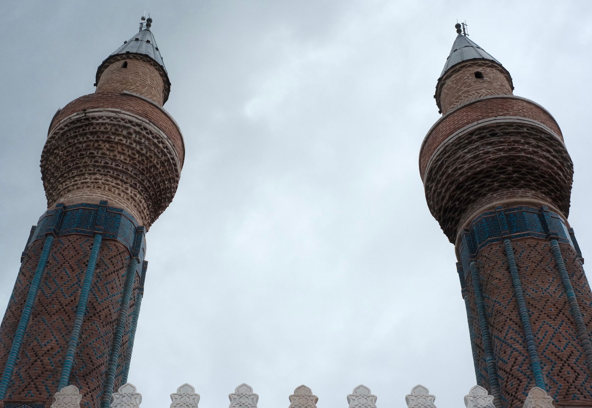 Dramatic twin minarets with intricate designs reach toward a cloudy sky, showcasing architectural beauty.