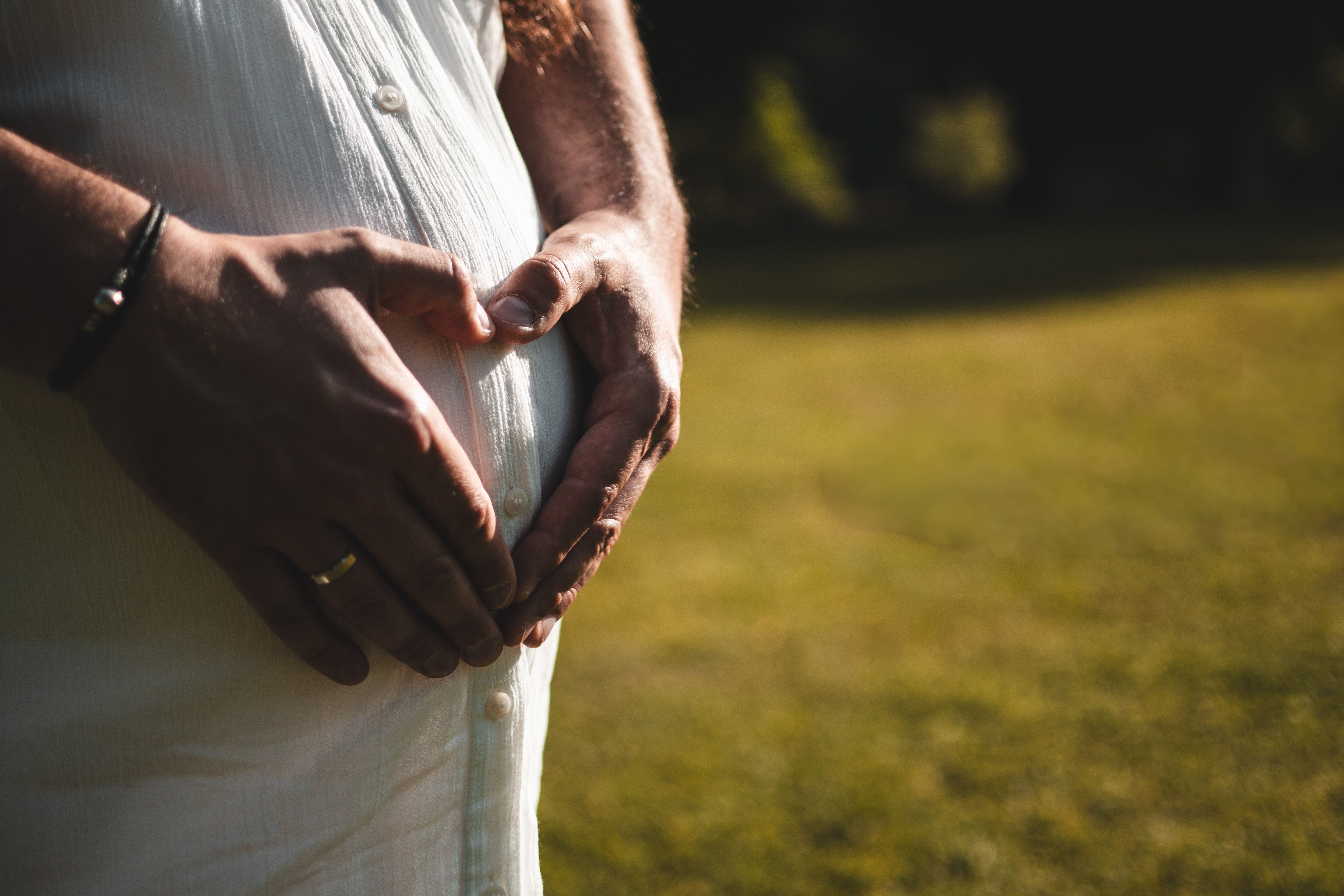 Pregnant woman gently holding her belly in a serene outdoor setting, symbolizing love and expectation.