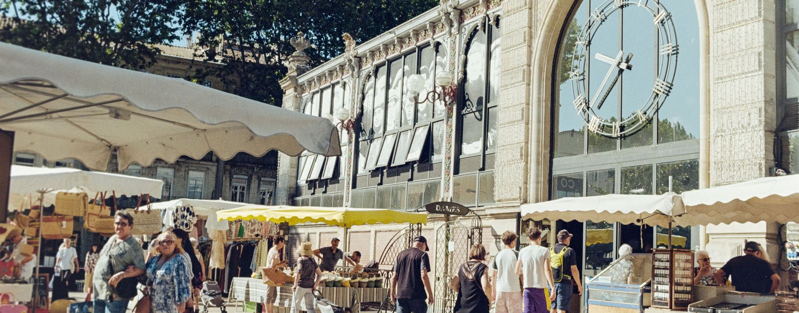 Lively outdoor market scene in Occitanie, France with people shopping under sunny skies.
