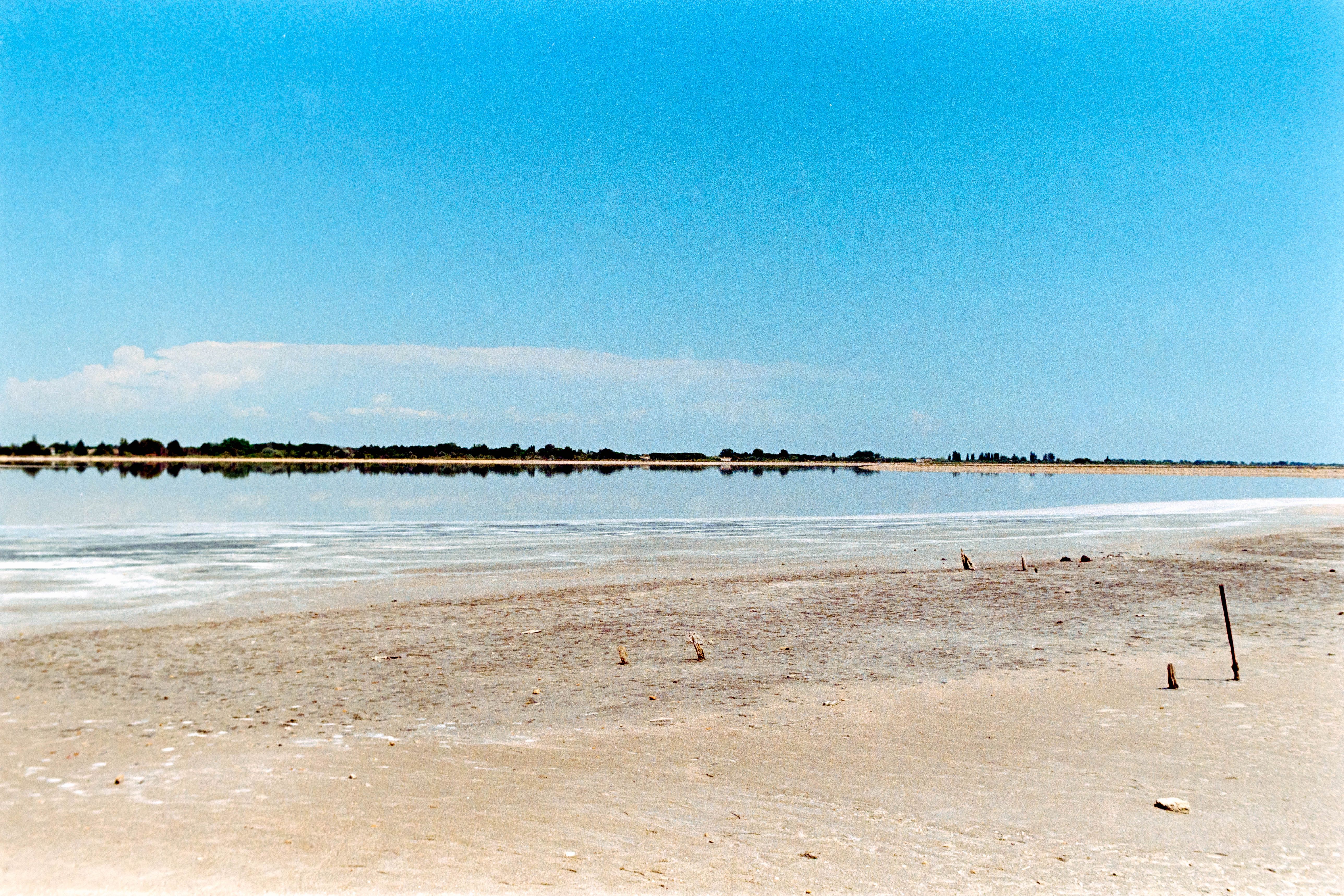 Peaceful sandy beach and calm blue water at Aigues-Mortes, Occitanie, France under a clear summer sky.