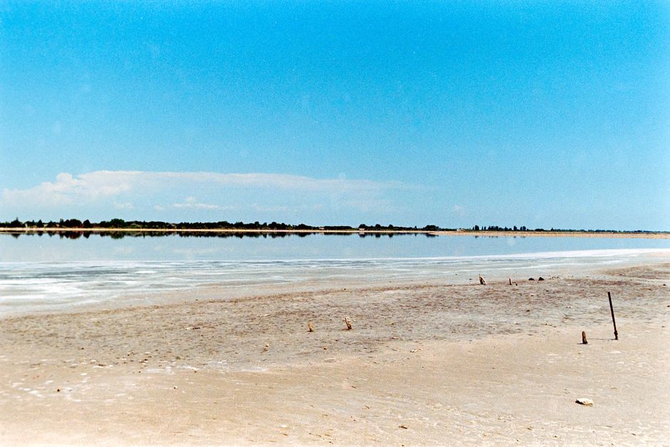 Peaceful sandy beach and calm blue water at Aigues-Mortes, Occitanie, France under a clear summer sky.
