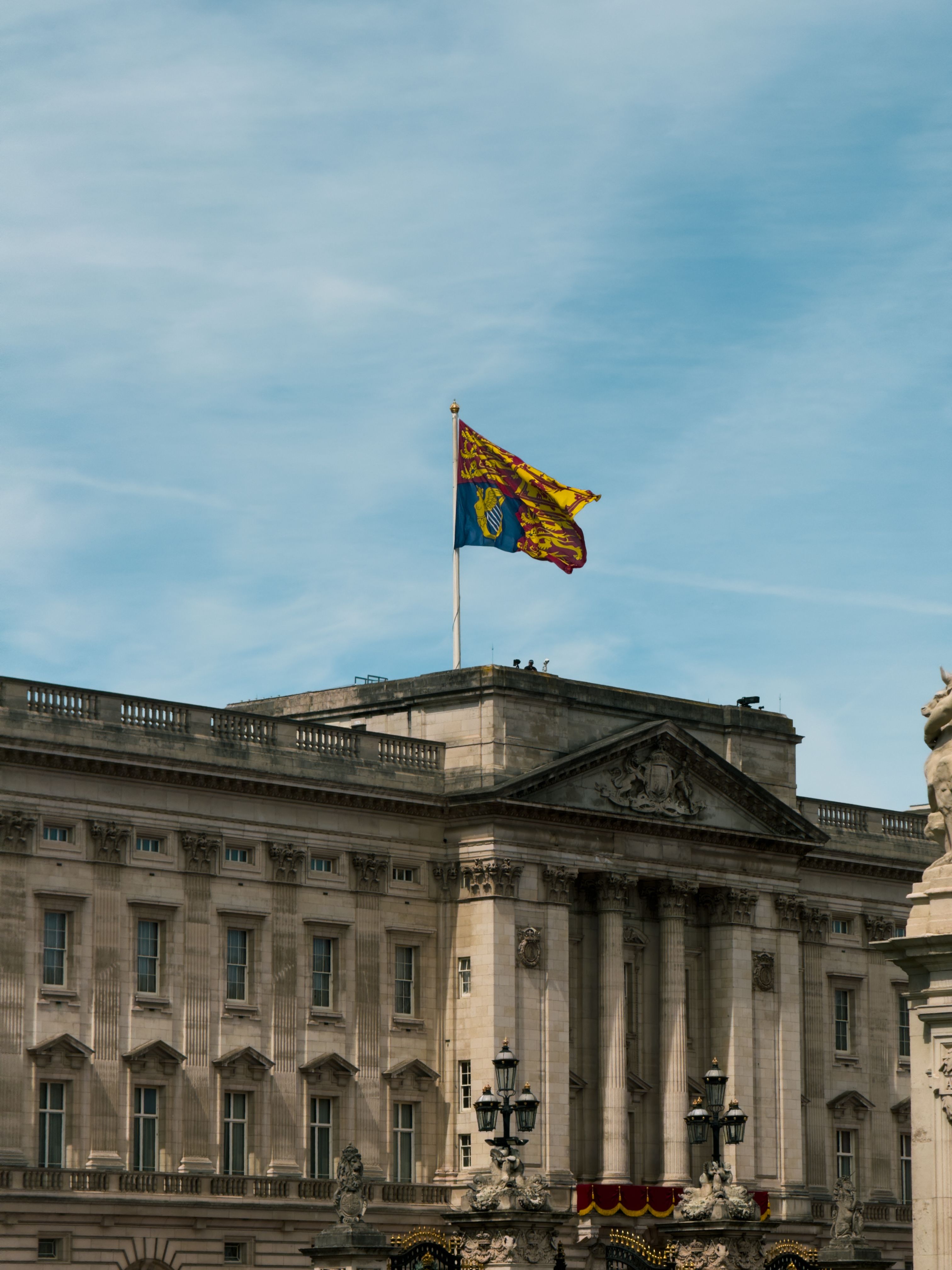 Iconisch uitzicht op Buckingham Palace met de koninklijke standaard hoog in de lucht, tegen een heldere hemel.