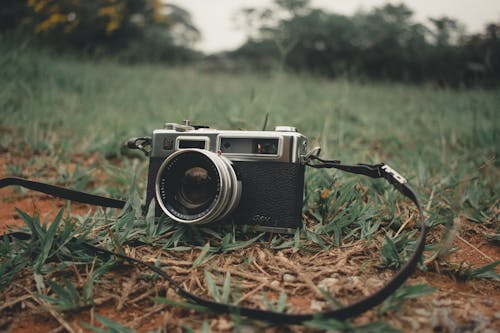 Vintage film camera with strap placed on ground with green grass in nature