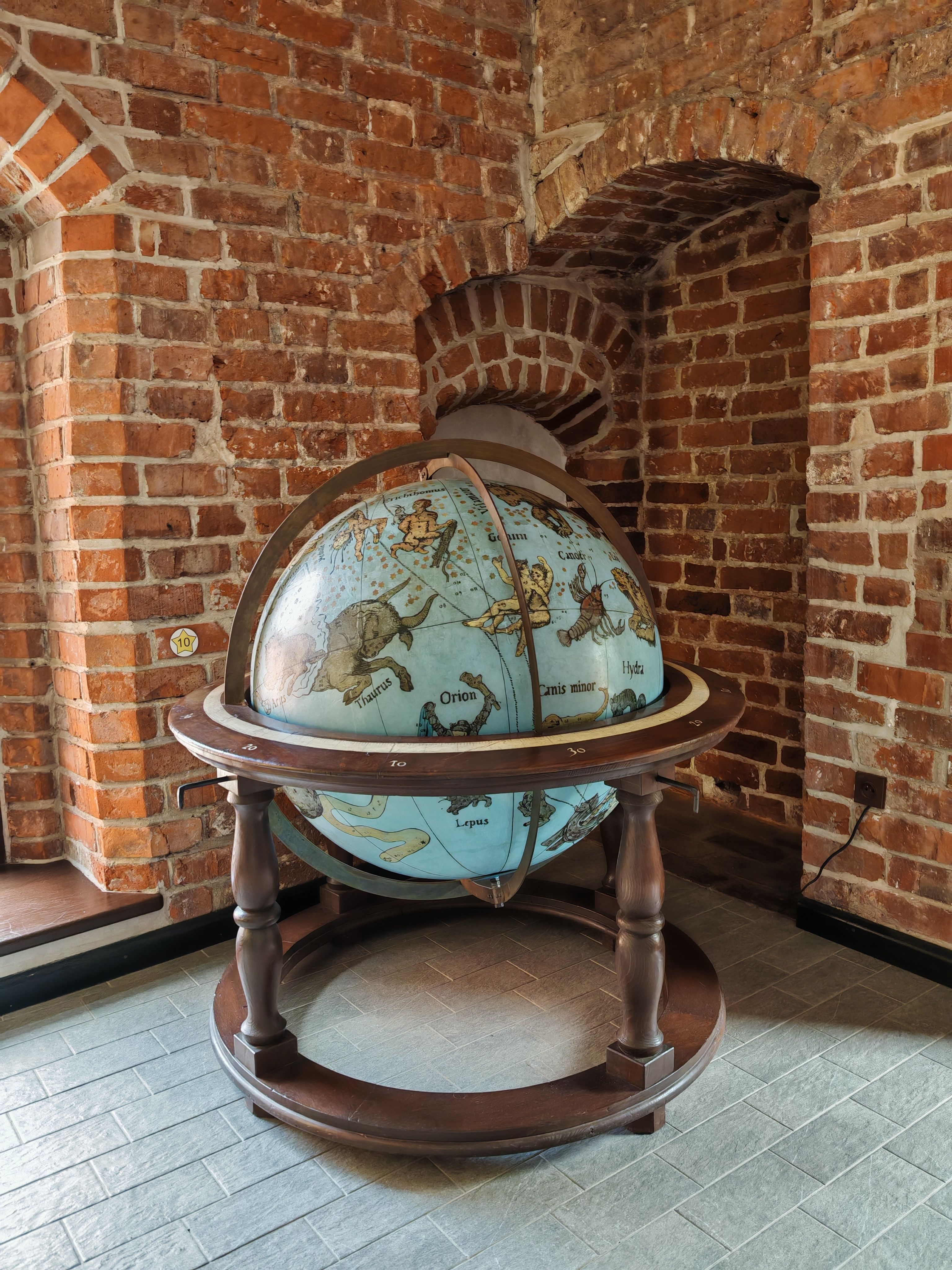 An antique celestial globe displayed in a rustic brick interior setting.