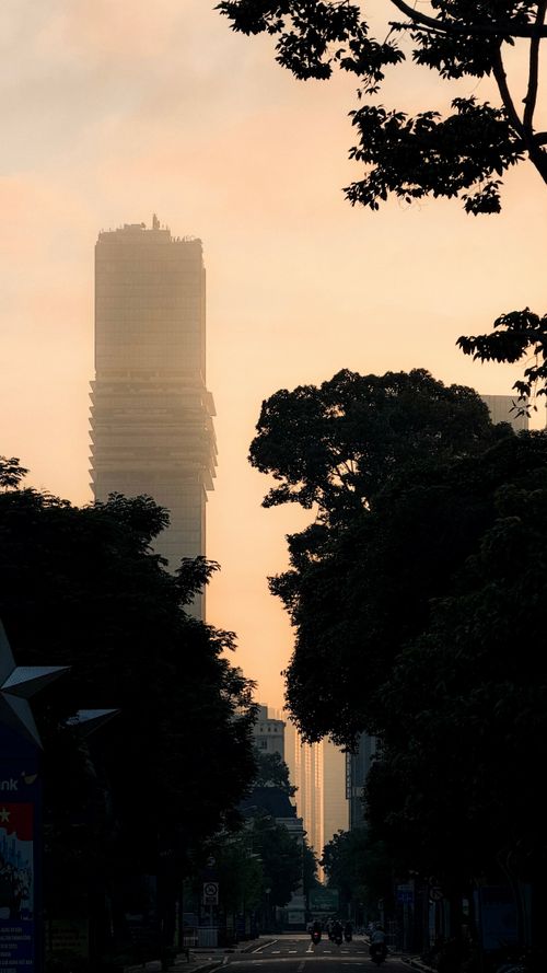 Free A silhouette of a tall building at sunset in Ho Chi Minh City with trees and skyline. Stock Photo