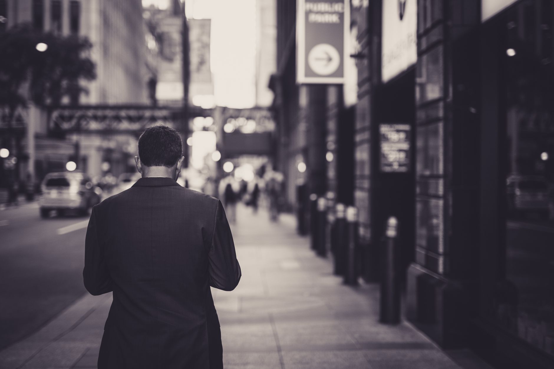 Man in a suit walking down a city street in a lonely, urban setting.