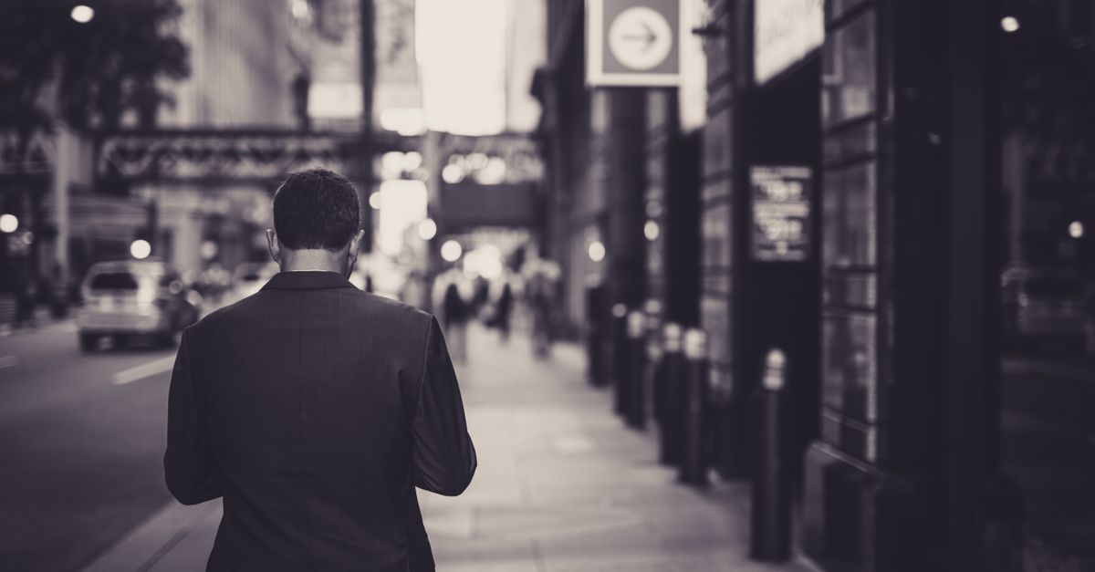 Man in a suit walking down a city street in a lonely, urban setting.