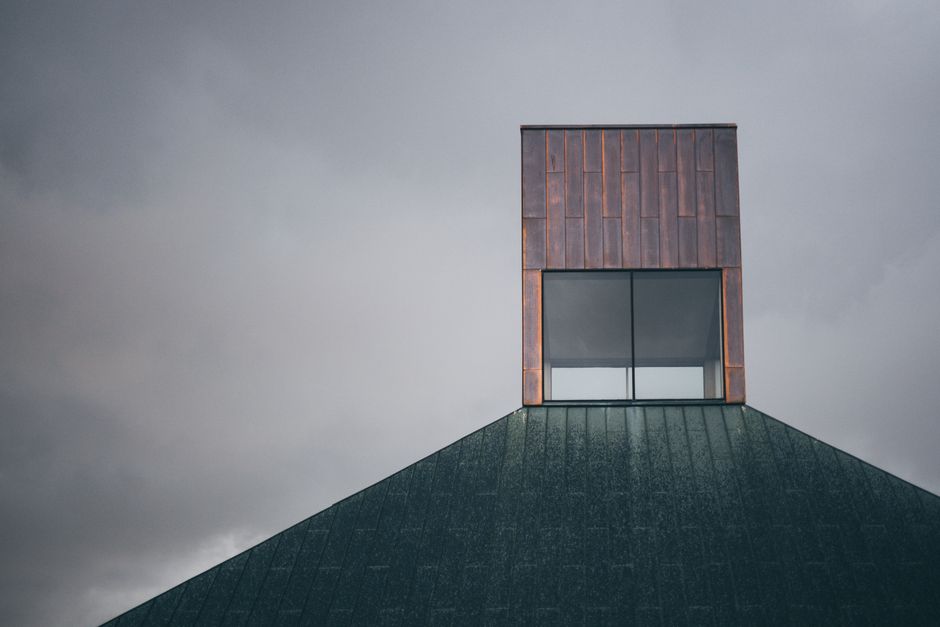 Minimalist architectural design featuring copper and glass elements against a cloudy sky.