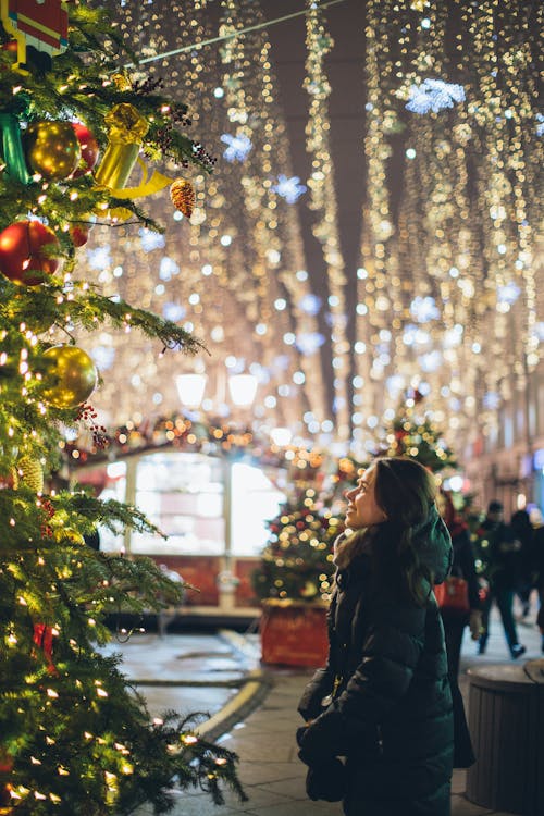 Woman in Black Coat Standing Beside Green Christmas Tree With String Lights