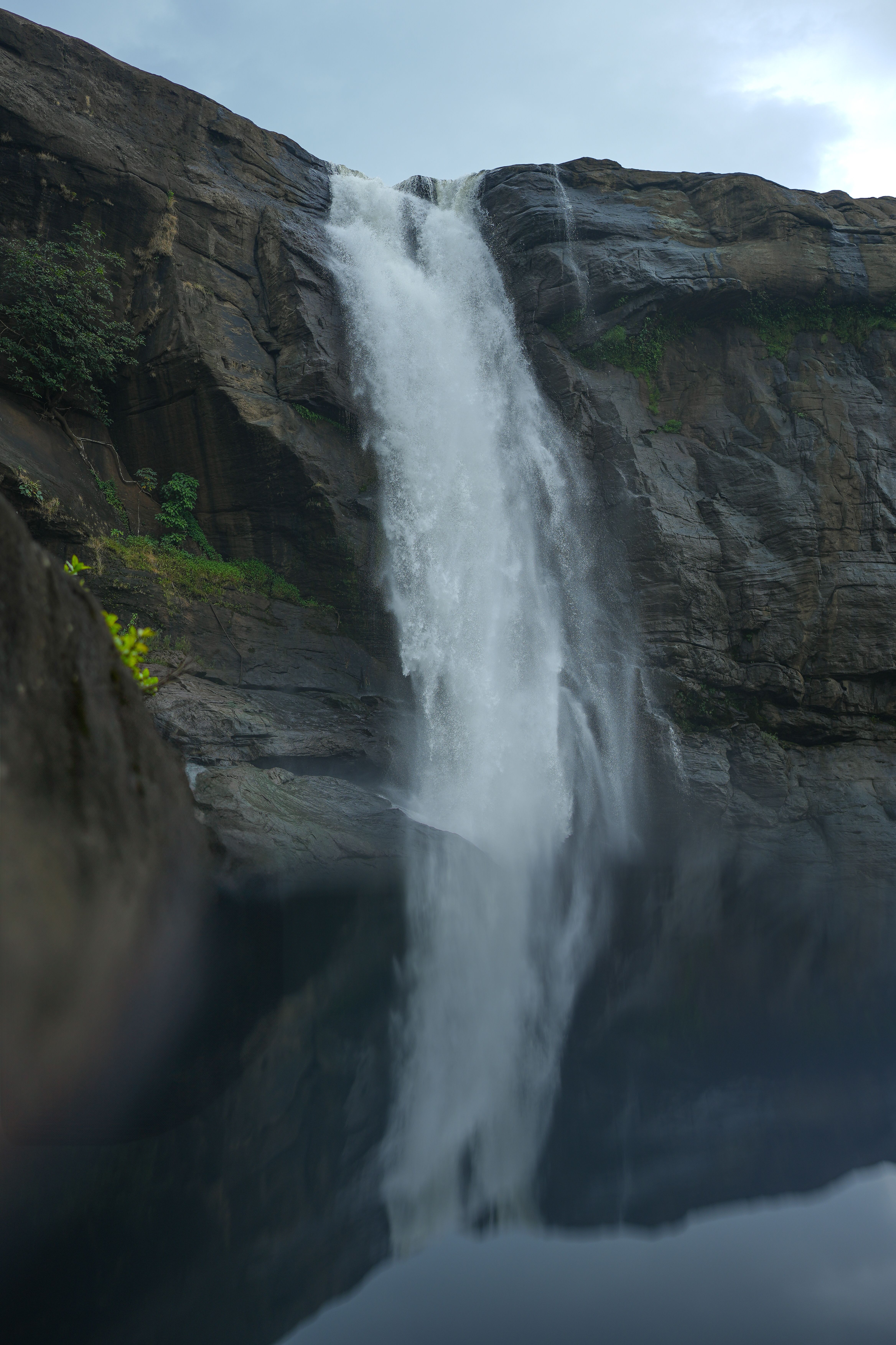 A stunning waterfall plunges into a serene pool, surrounded by rocky cliffs and lush greenery.