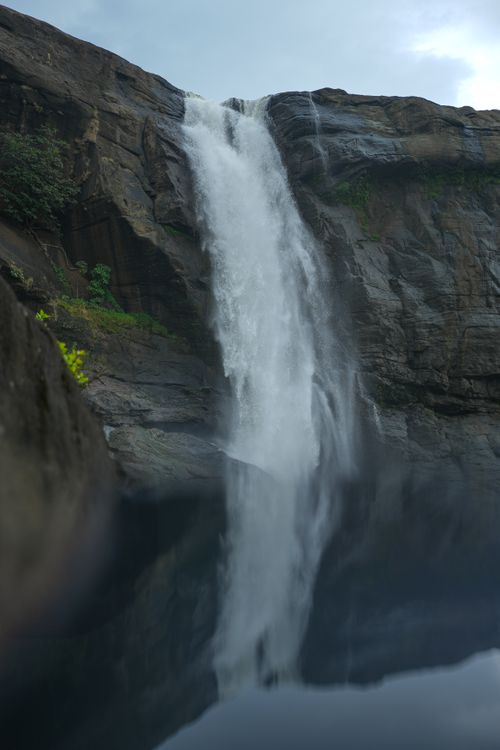 Free A stunning waterfall plunges into a serene pool, surrounded by rocky cliffs and lush greenery. Stock Photo