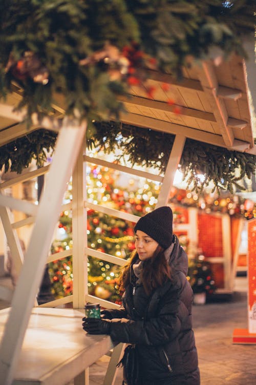 Woman in Black Knit Cap and Black Jacket Standing Near White Table