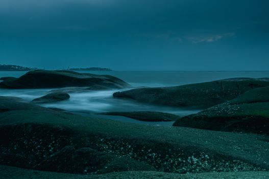 Misty twilight ocean scene with dark rock formations, capturing tranquility.