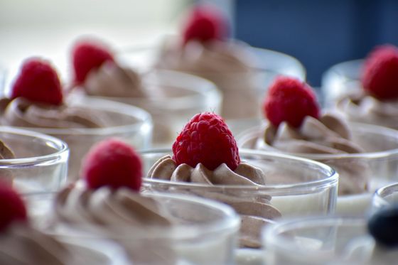Rows of small glasses filled with piped milk chocolate mousse, each topped with a raspberry