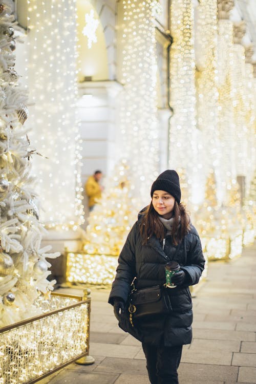 Woman in Black Jacket and Black Knit Cap Standing Near White Christmas Tree