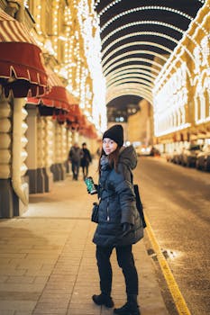 Woman in winter clothing walking along a beautifully illuminated street, holding a drink.