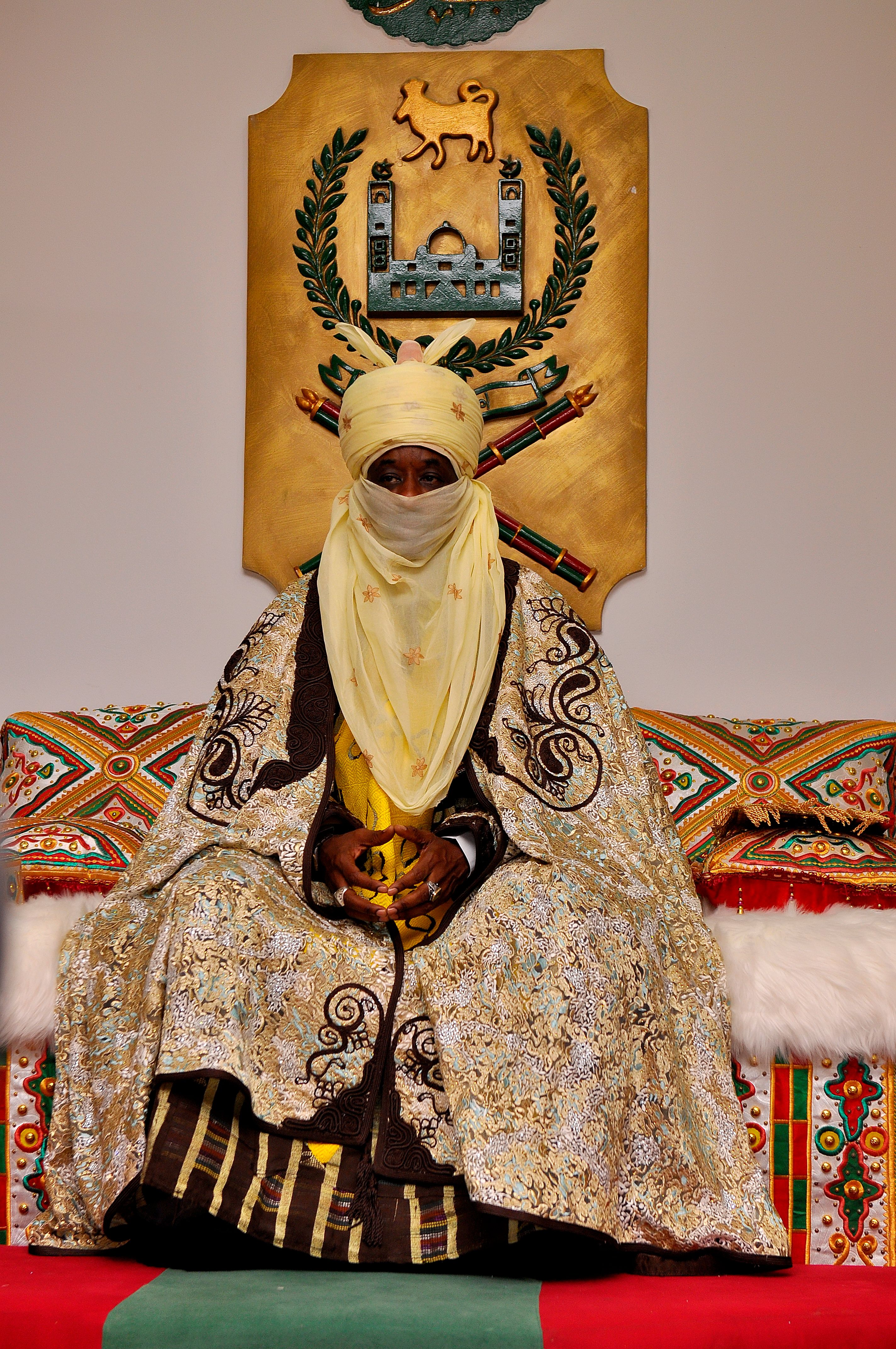 A Nigerian Emir sits on a throne in Kano, showcasing ornate cultural attire.