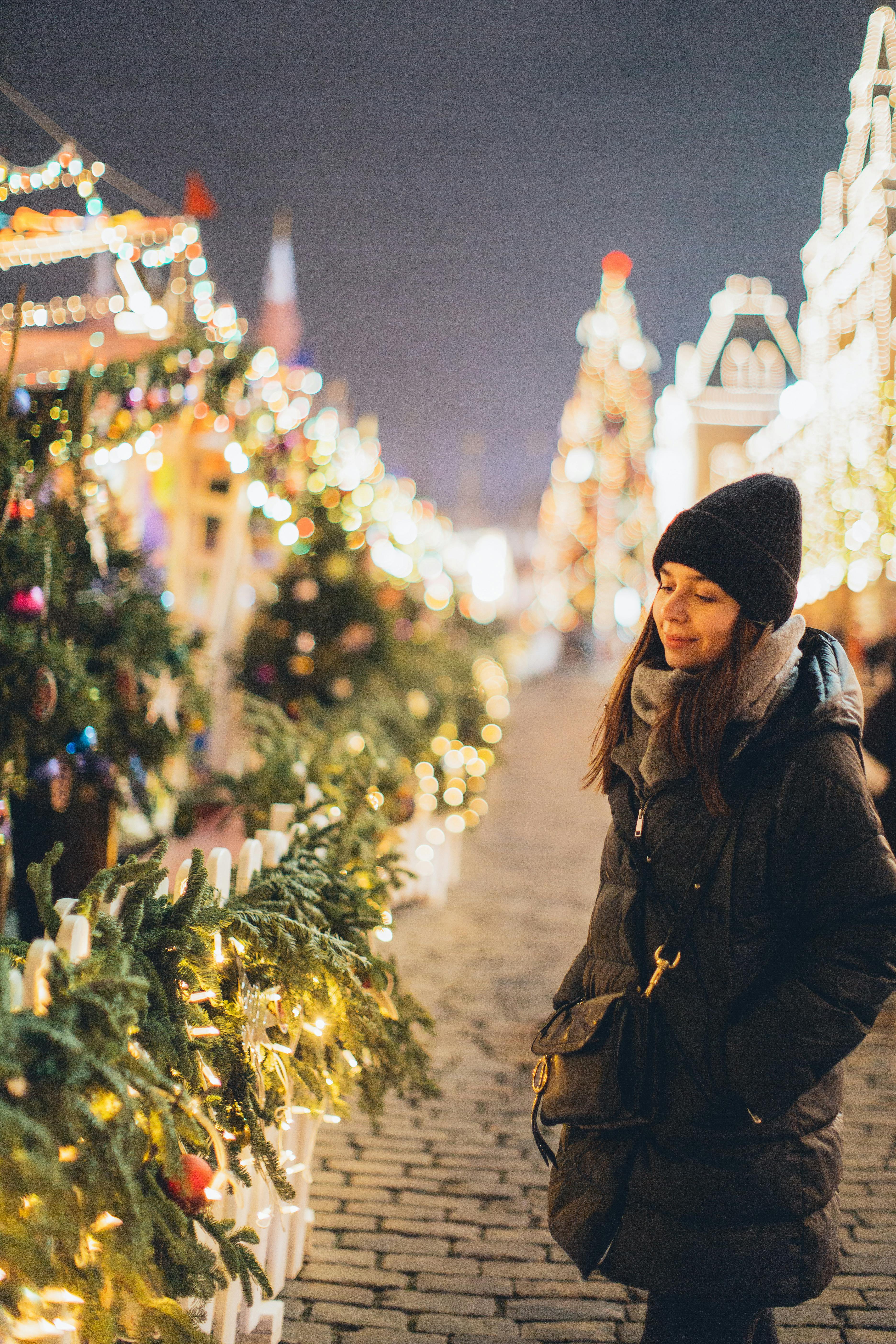 一位穿着冬装的妇女在户外圣诞市场微笑着享受节日灯光