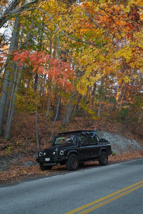 Free A black SUV parked by a scenic road during vibrant autumn foliage. Stock Photo