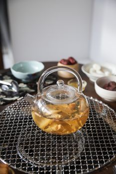 Glass teapot with herbal tea and dried ingredients on a kitchen counter, warm ambiance.