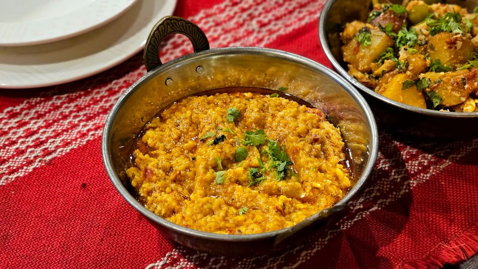 A bowl of golden-orange red lentil dal topped with a fried cumin and mustard seed tadka, chopped cilantro, and a lemon wedge, served with rice on the side.