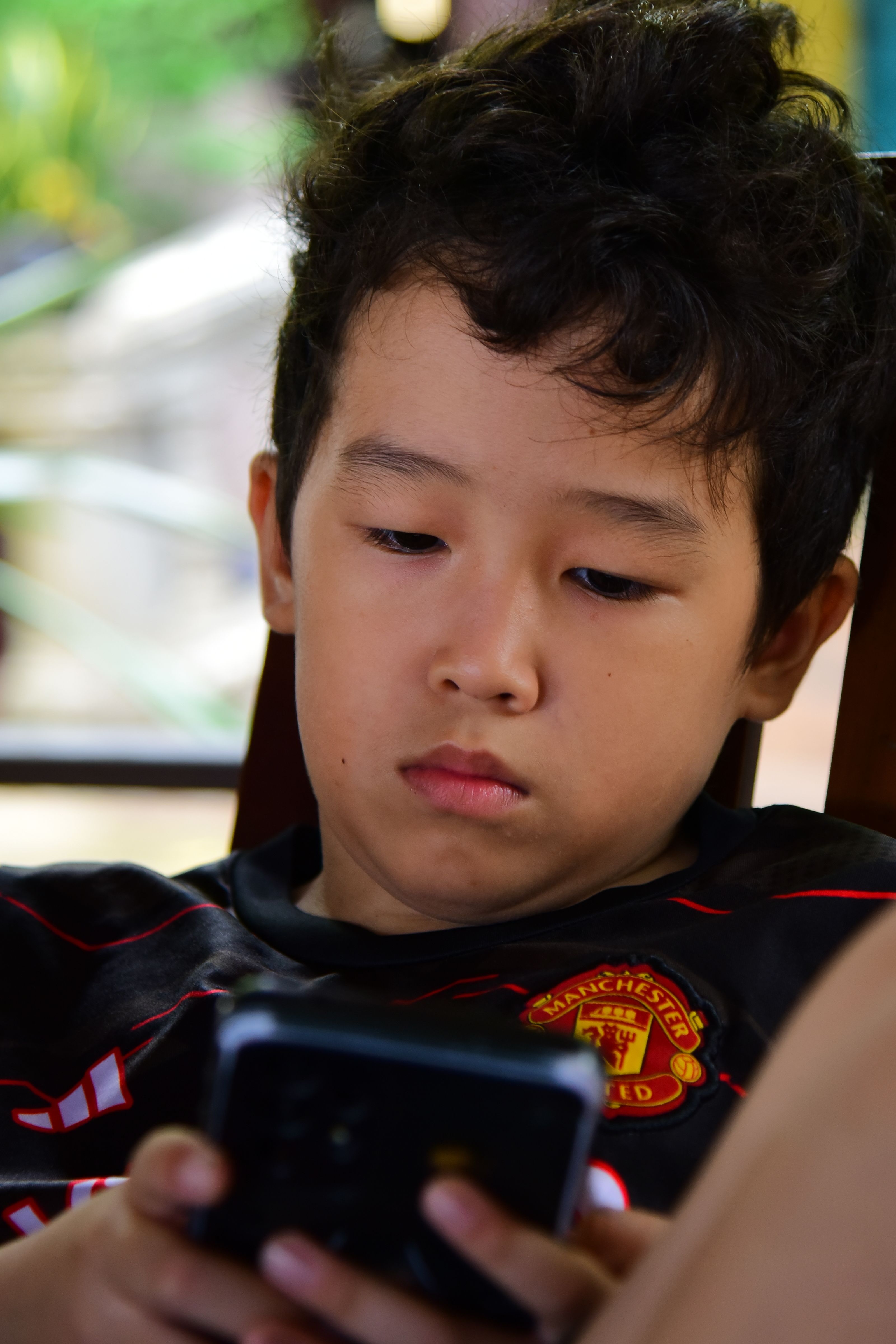 A young boy engrossed in his smartphone indoors, representing modern digital lifestyle.