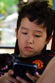 A young boy engrossed in his smartphone indoors, representing modern digital lifestyle.