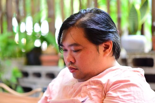 Free A thoughtful man enjoying a quiet moment in a lush garden, surrounded by green plants. Stock Photo