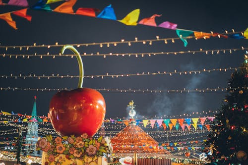 Free Big red glossy toy apple on roof of building on fairground against dark sky in evening city park decorated to winter holidays Stock Photo