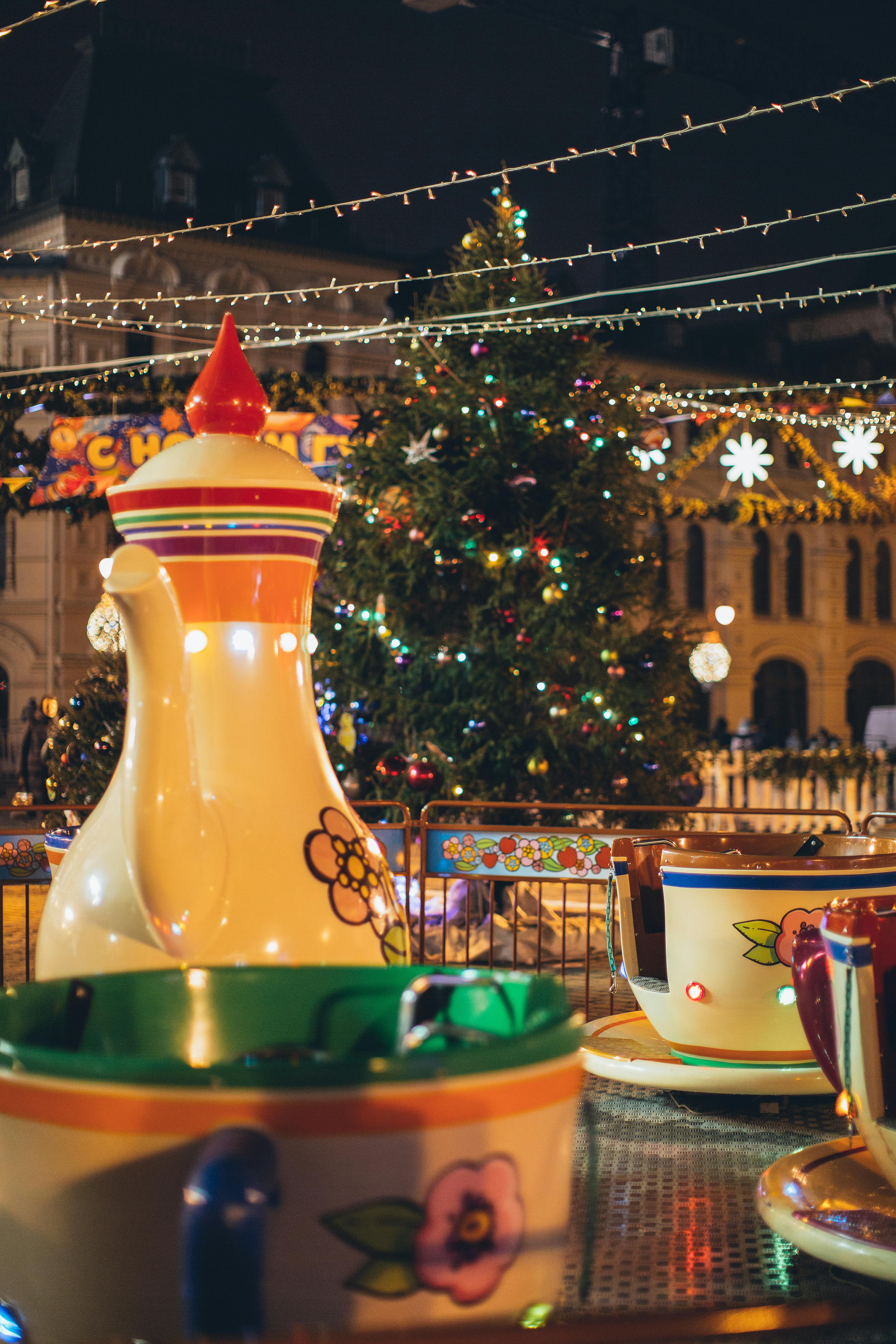 Free Merry go round with large colorful traditional Russian teapot and cups in city park decorated in New Year style in evening Stock Photo