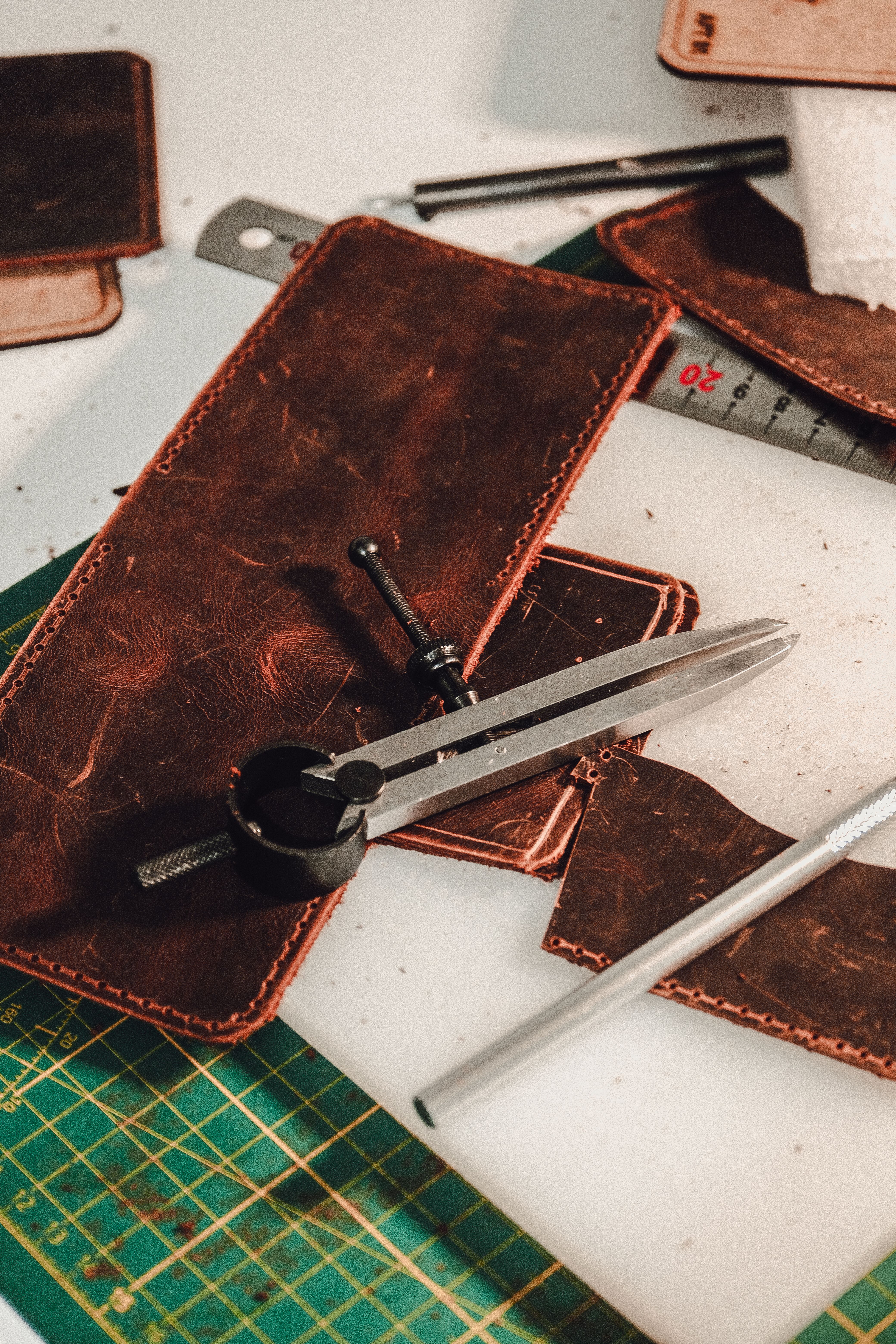 Close-up of leather crafting tools and materials on a workbench, featuring a divider and leather pieces.