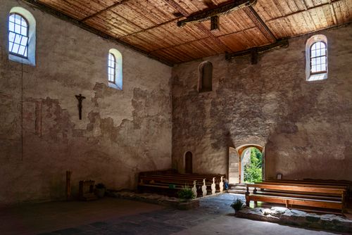 Free Sunlit interior of an ancient stone chapel with wooden benches and rustic walls. Stock Photo