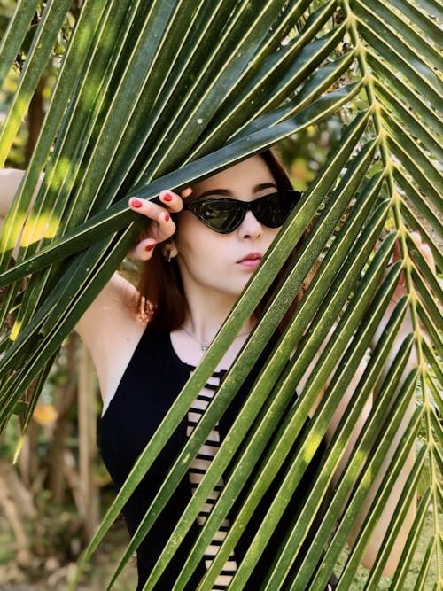 Стильная женщина прячется за пальмовым листом