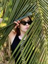 Stylish woman hiding behind palm leaf