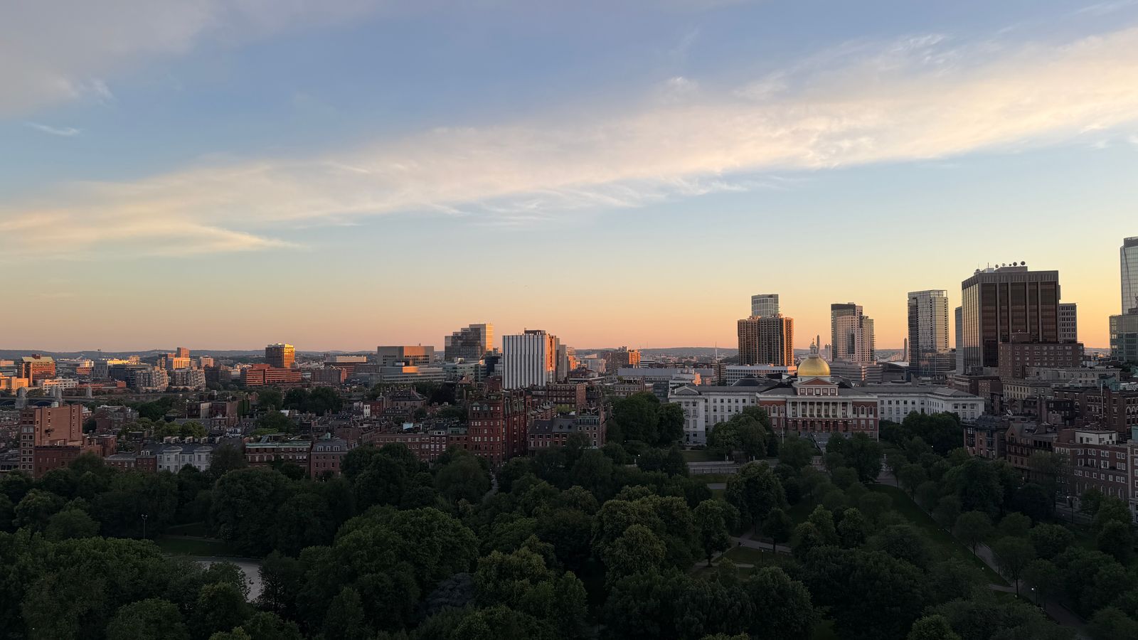 Aerial view of Boston skyline at sunset, featuring lush greenery and city buildings.