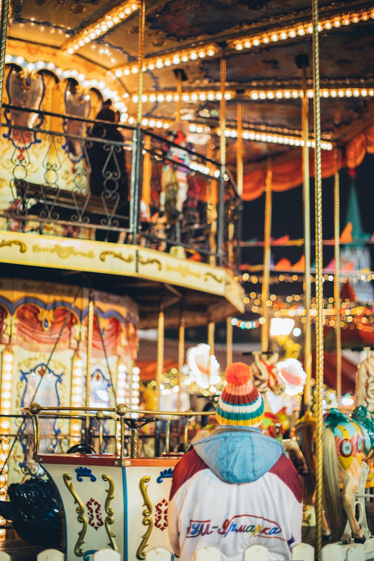 Person Watching Luminous Festive Carousel In Amusement Park At Night