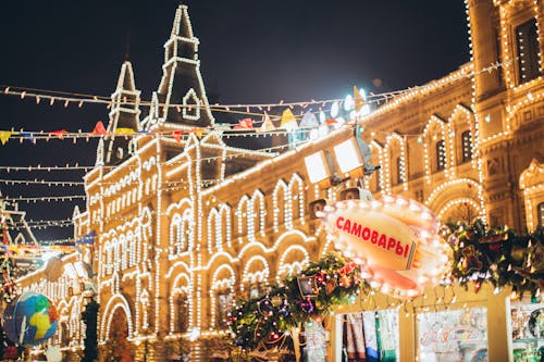 Low angle of exterior of old building decorated with small round white lamps during Christmas holiday in night city under cloudy dark sky